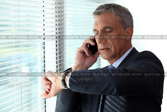 Businessman checking time whist on telephone call. Стоковое фото, агентство Ingram Publishing / Фотобанк Лори