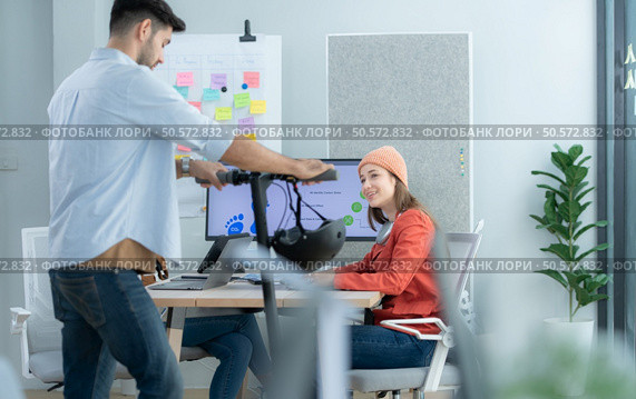 Businessman riding electric scooter in office with colleague in background. Стоковое фото, агентство Ingram Publishing / Фотобанк Лори