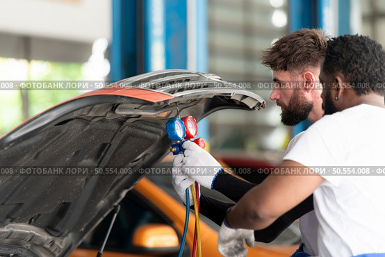 Car mechanic working in an auto repair shop, inspecting the operation of the car’s air conditioner and refrigerant. Стоковое фото, агентство Ingram Publishing / Фотобанк Лори