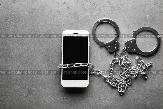 Chained mobile phone with handcuffs on grey table. Concept of addiction. Стоковое фото, фотограф Pixel_shot / Фотобанк Лори