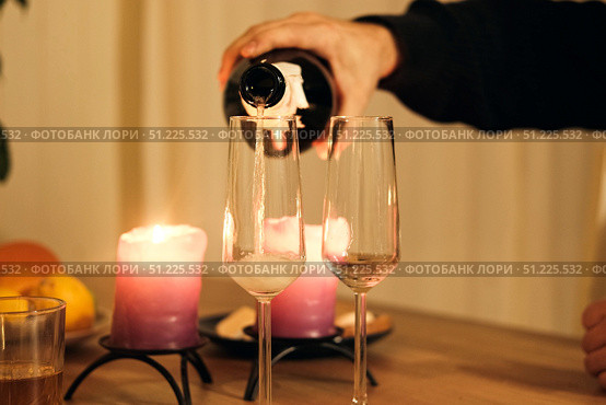 Champagne being poured into champagne flute, bubbles. Sparkling beverage. Romantic Dinner Table with Flickering Candles, Flutes. Warm ambiance. Glasses of champagne. Celebration, Anniversary, Luxury. Стоковое фото, фотограф Марина Демидюк / Фотобанк Лори