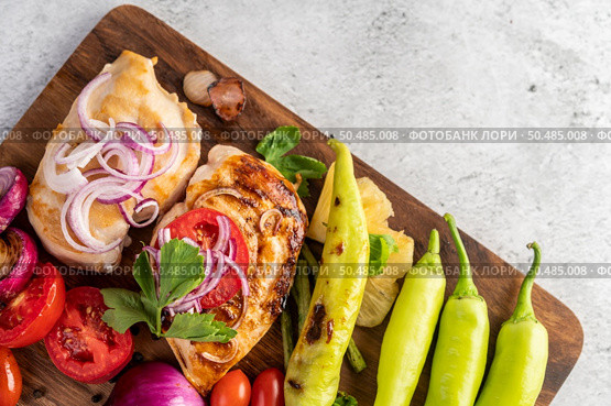 Chicken steak placed on a wooden tray with bell peppers, tomatoes, red onions, pineapple sauce, lettuce, and sesame seeds. Стоковое фото, агентство Ingram Publishing / Фотобанк Лори
