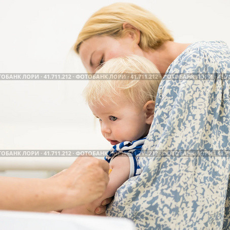 Child beeing vaccinated by pediatrician in presence of his mother. Preventive vaccination against Diphtheria, whooping cough, tetanus, hepatitis, haemophilus influenzae, pneumococcus, poliomyelitis. Стоковое фото, фотограф Matej Kastelic / Фотобанк Лори