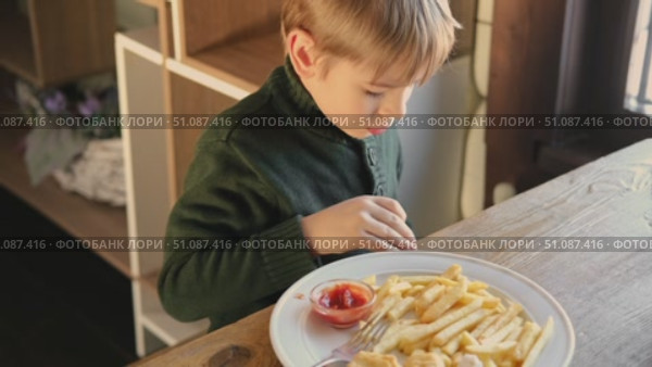 Child Eating French Fries with Tomato Sauce in Restaurant Indoors. Little Kid with Blond Hair Enjoy Unhealthy Fast Food. lunch. Caucasian Boy Eats Potato Chips at the Table. Three or Six Years Old. Стоковое видео, видеограф Марина Демидюк / Фотобанк Лори
