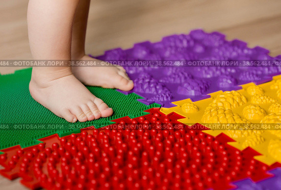 Child feet on orthopedic baby massage puzzle floor mats with colorful details for preventing flatfoot. Стоковое фото, фотограф Photojuli / Фотобанк Лори