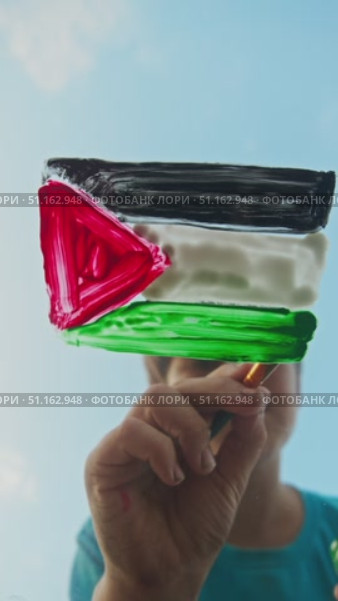 Child paints flag of Palestine in bright colors on glass against background of serene azure sky, embodying security and serenity. Стоковое видео, видеограф Strunov David / Фотобанк Лори