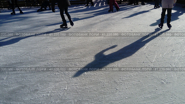 Children ride in a city park on an ice rink. Feet skater while skating on ice. The low winter sun weakly illuminates the ice. Dark shapes and long shadows on the surface. Sports movements. Стоковое фото, фотограф Юлия Петровская / Фотобанк Лори