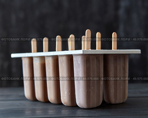 Chocolate ice cream lolly sorbet in a mold on a black wooden table. Cold dessert. Coffee ice cream on a stick in plastic molds on a dark wooden background. Summer dessert. Стоковое фото, агентство Ingram Publishing / Фотобанк Лори