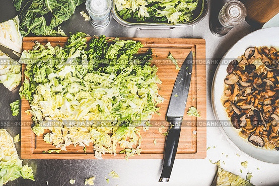 Chopped savoy cabbage on cutting board with kitchen knife and pan with mushrooms. Vegetarian cooking concept. Стоковое фото, агентство Ingram Publishing / Фотобанк Лори