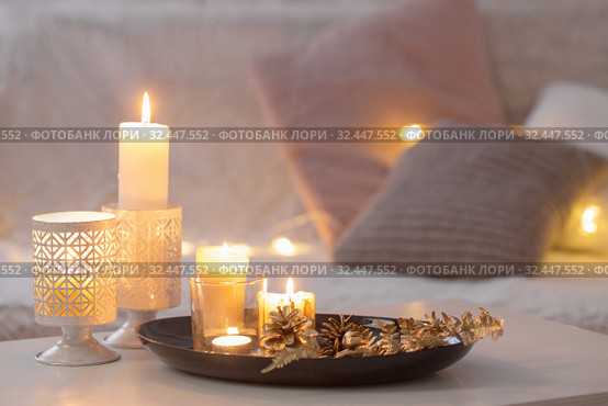 Christmas decoration with burning candles on white table against the background of sofa with plaids and pillows. Cozy home and holiday concept. Стоковое фото, фотограф Майя Крученкова / Фотобанк Лори