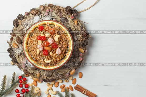 Christmas porridge with nuts and candied fruits. In the center of the wreath of cones and fir branches. On a light wooden background with space. Стоковое фото, фотограф Bogdanova Mariia / Фотобанк Лори