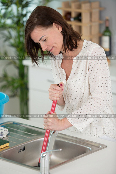 cleaning clogged pipes in the kitchen sink with a plunger. Стоковое фото, агентство Ingram Publishing / Фотобанк Лори