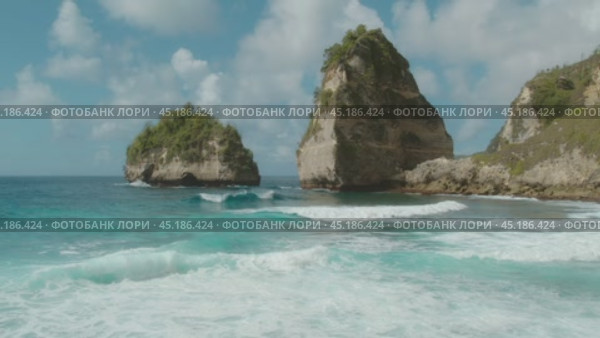 Clear blue waves crash against the towering cliffs covered with lush vegetation, creating a serene natural seascape. Стоковое видео, видеограф Igor Tichonow / Фотобанк Лори