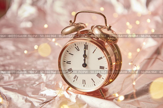 Close up golden painted alarm clock with Christmas time is midnight on a shiny cooper abstract background with garland, copy space. Greeting card.. Christmas card with golden alarmclock and garland. Стоковое фото, агентство Ingram Publishing / Фотобанк Лори