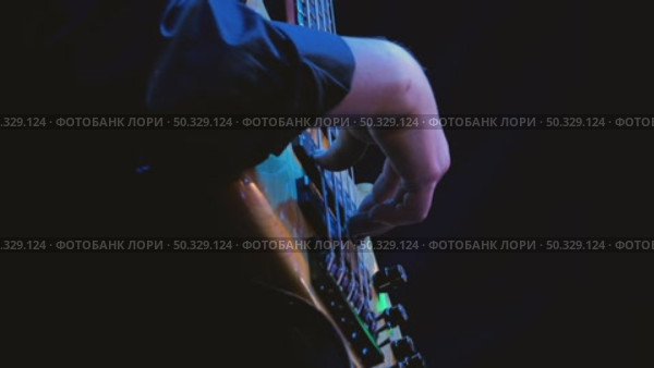 Close-up of a bassist's hand, playing bass guitar professionally, illuminated by soft multicolored stage lights against a dark background. Fingers skillfully plucking the strings. Стоковое видео, видеограф Воловодов Владимир / Фотобанк Лори