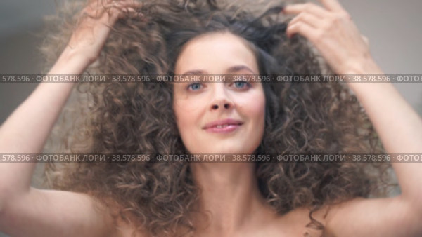 Close-up of a beautiful young woman with curly hair, she tilts her head in different directions, smiling at the camera, touching her hair with her hands. Стоковое видео, видеограф Darya Komarova / Фотобанк Лори