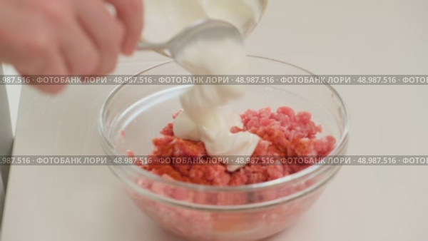 Close-up of a hand adding sour cream to a bowl of raw ground meat, preparing ingredients for a home-cooked meal. Стоковое видео, видеограф Андрей Журавлев / Фотобанк Лори
