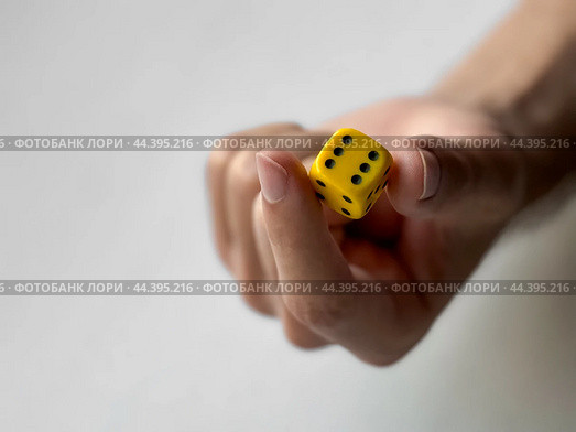 Close-up of hand holding yellow dice with black dots on minimalist background. Стоковое фото, фотограф Lamina Akulova / Фотобанк Лори