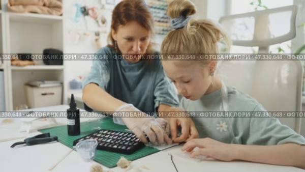 Close-up of hands creating custom jewelry with resin. Child and parent work together, pouring vibrant resin into tiny molds. Handmade art project helps develop creativity, patience, fine motor skills. Стоковое видео, видеограф Енваев Андрей / Фотобанк Лори