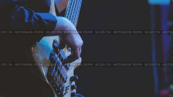 Close-up of skillful bass guitar playing during a live concert. Dark background enhances the focus on the instrument and the performer's technique, while soft blue lighting emphasizes the scene. Стоковое видео, видеограф Воловодов Владимир / Фотобанк Лори