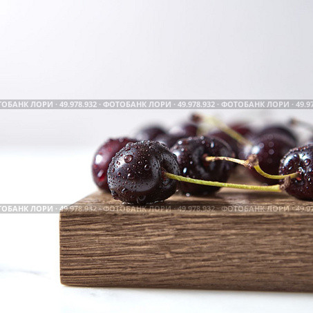 Close-up ripe organic natural cherry in water droplets on a wooden board on white background with soft focus. Copy space.. Home grown fresh cherry with shallow depth of field. Ingredients for sweet homemade jam on a board. Стоковое фото, агентство Ingram Publishing / Фотобанк Лори