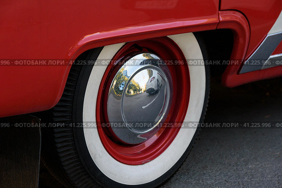 Closeup photo of the rear wheel of a magnificent retro car. The wheel has a red stamped disc in the body color, a large chrome hood and white wall. Фотография заднего колеса великолепного ретро-автомобиля крупным планом. Колесо имеет красный штампованный диск в цвет кузова, большой хромированный колпак и белую каемку. Стоковое фото, фотограф Дмитрий Березнев / Фотобанк Лори