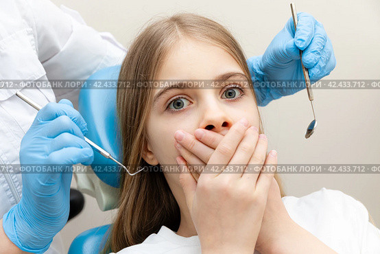 Closeup terrified girl woman scared at dentist visit, siting in chair, covering mouth, doesn't want dental procedure, drilling, tooth extraction, clinic office background. Fear of dentists. Toothache. Стоковое фото, фотограф Ирина Михайличенко / Фотобанк Лори
