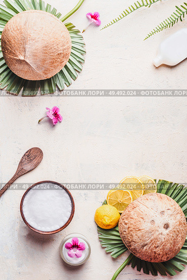 Coconut oil in wooden bowl with spoon and moisturizing cream on white desk background with tropical leaves and flowers , top view. Frame. Copy space. Flat lay. Modern skin care and cosmetic concept. Стоковое фото, агентство Ingram Publishing / Фотобанк Лори