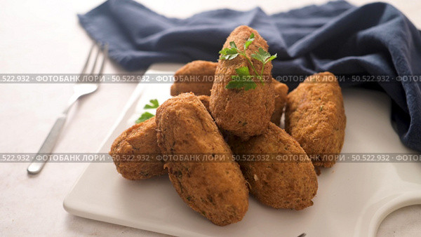 Cod dumplings, or "bolinhos de bacalhau" and parsley leaves on white ceramic dishes in a kitchen counter top. Стоковое фото, агентство Ingram Publishing / Фотобанк Лори