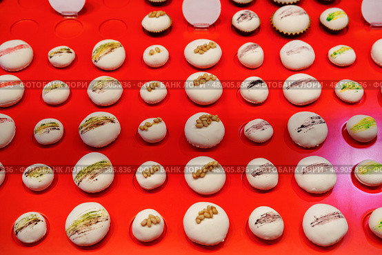 Colorful macarons arranged neatly on a bright red display reflecting an artful pastry shop environment. Стоковое фото, фотограф Сергей Толмачёв / Фотобанк Лори