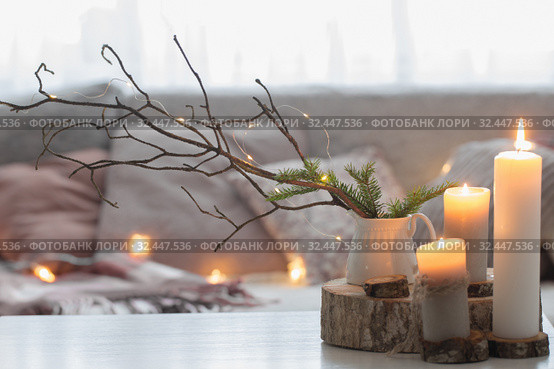 Composition of candles on white table against the background of sofa with plaids and pillows. Cozy home concept. Стоковое фото, фотограф Майя Крученкова / Фотобанк Лори