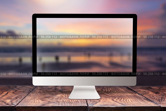 Computer display with sunset sea blurred picture on a wooden table against the same background with bokeh, copy space. Working remotely at seacoast, on nature, outside office concept.. Computer screen with blurred sea background. Стоковое фото, агентство Ingram Publishing / Фотобанк Лори