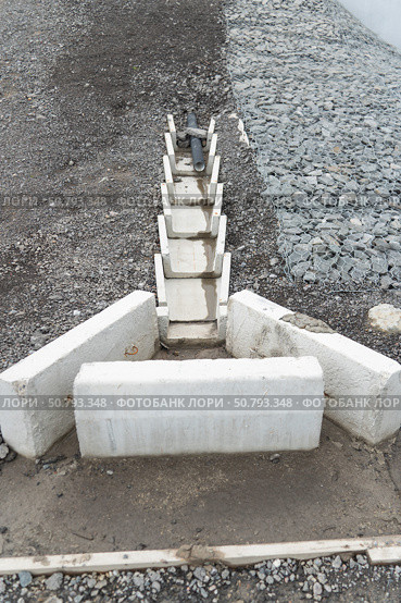 Concrete drainage channel with embedded plastic pipe for stormwater management, set against gravel and gabion-covered slope. Стоковое фото, фотограф Софья Соломонова / Фотобанк Лори