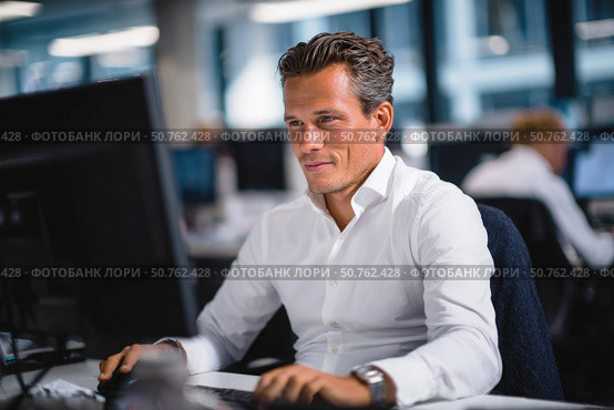 Confident businessman working on desktop computer in modern office environment, wearing white shirt and focused on task with professional demeanor. Стоковое AI-изображение, AI-художник Катерина Бондарец / Фотобанк Лори