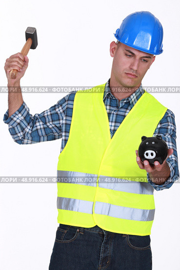 Construction worker breaking open a piggy bank. Стоковое фото, агентство Ingram Publishing / Фотобанк Лори
