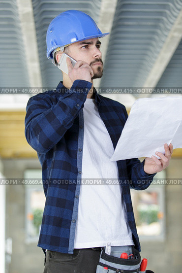 contractor on site holding plans and making telephone call. Стоковое фото, агентство Ingram Publishing / Фотобанк Лори