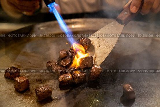 Cooking of beef teppanyaki recipe japanese grilled beef on cooking pan with scraper and gas burner flame. Стоковое фото, агентство Ingram Publishing / Фотобанк Лори