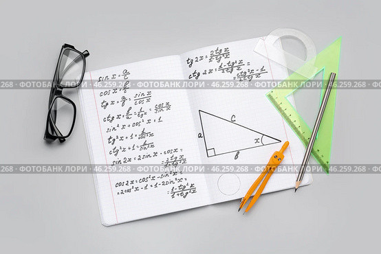 Copybook with maths formulas, glasses and stationery on grey background. Стоковое фото, фотограф Pixel_shot / Фотобанк Лори