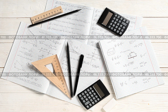Copybooks with handwritten maths formulas, calculators and stationery on white wooden background. Стоковое фото, фотограф Pixel_shot / Фотобанк Лори