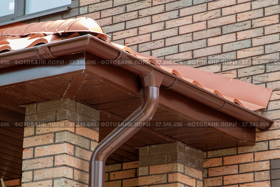 Corner of house with new brown metal tile roof and rain gutter. Metallic Guttering System, Guttering and Drainage Pipe Exterior. Стоковое фото, фотограф Данила Большаков / Фотобанк Лори
