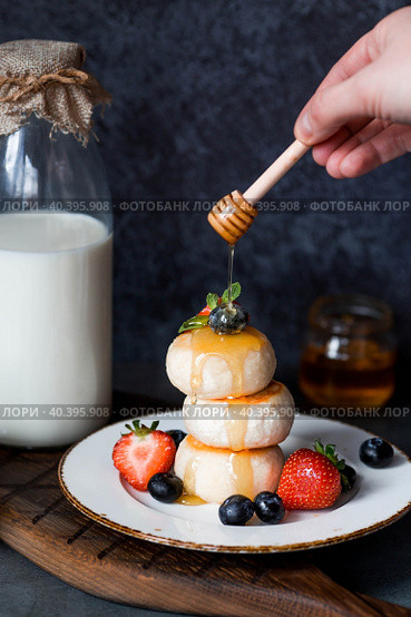 Cottage cheese pancakes, Russian cheesecakes with fresh blueberries, strawberries, honey and mint leaves on a stylish wooden board on a dark background. Natural products. Healthy and delicious breakfast. Стоковое фото, фотограф Photojuli / Фотобанк Лори