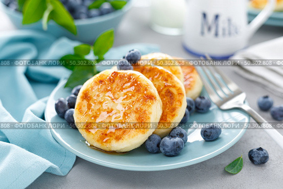 Cottage cheese pancakes, sweet curd fritters with berries, syrniki with honey and fresh blueberry on breakfast table. Стоковое фото, агентство Ingram Publishing / Фотобанк Лори