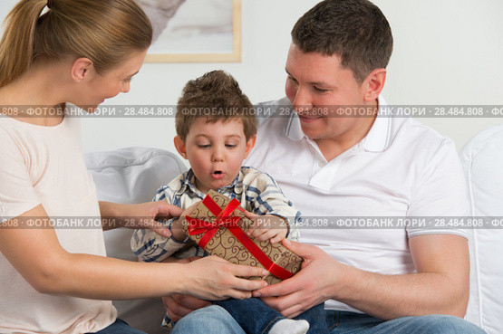 Couple giving gift to their little son in the living room. Happy family portrait. Стоковое фото, фотограф Kirill Kedrinskiy / Ingram Publishing / Фотобанк Лори