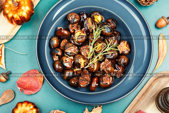 Cracked roasted chestnuts, roasted chestnuts some chestnuts split open , garnished with fresh rosemary, styled with autumn leaves.. Warm roasted chestnuts served on a plate. Стоковое фото, агентство Ingram Publishing / Фотобанк Лори