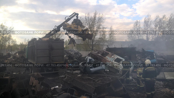 Crane lifting debris at a scrapyard during daylight cleanup operation with firefighters present. Стоковое фото, фотограф Александра Рублева / Фотобанк Лори