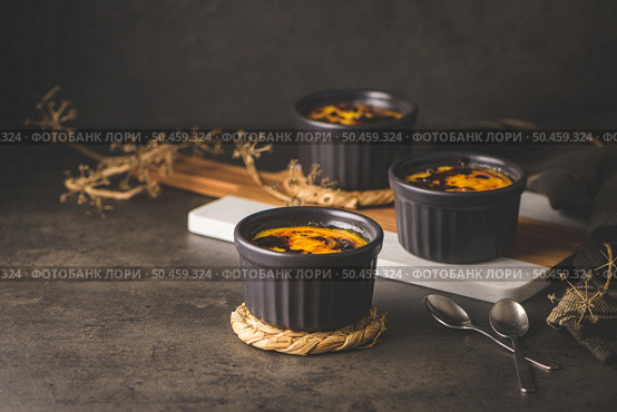 Creme brulee. Bowls with French vanilla cream dessert with caramelised sugar on top, spoons, dark rustic table. Стоковое фото, агентство Ingram Publishing / Фотобанк Лори