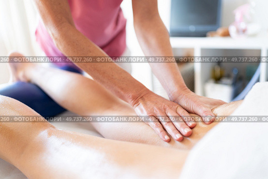Crop female therapist rubbing oily leg of female client lying on stomach over spa table during physiotherapist massage session in clinic. Crop masseuse rubbing oily skin of client during body massage in clinic. Стоковое фото, агентство Ingram Publishing / Фотобанк Лори