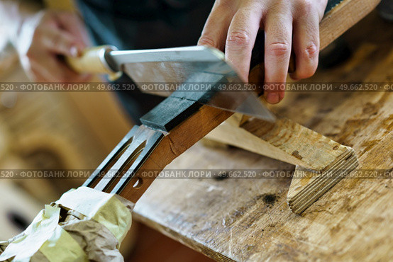 Crop male artisan using sharp knife to cut wood, marking the frets on neck of Spanish flamenco guitar during work in professional luthier workshop. Unrecognizable luthier cutting guitar neck marking the frets. Стоковое фото, агентство Ingram Publishing / Фотобанк Лори