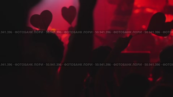 Crowd of concertgoers holding heart-shaped signs in vibrant red lighting atmosphere. Стоковое видео, видеограф Данил Руденко / Фотобанк Лори