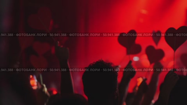 Crowd of hands holding red heart-shaped signs at a vibrant concert with dramatic lighting effects. Стоковое видео, видеограф Данил Руденко / Фотобанк Лори